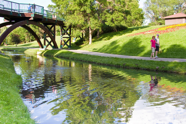 Two people walking beside a river in Moose Jaw in the summertime