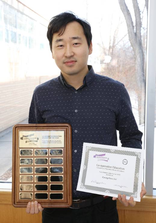 Kyoungcheon Choi close-up, holding his two awards plaques.