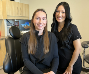 Two dental assisting students sitting on a dental chair smiling for the camera