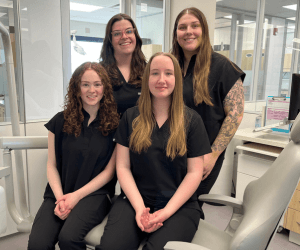 Four second year dental hygiene students sitting in the dental office with two on a chair and two standing