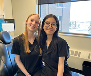 Four students wearing black scrubs sitting on a dental chair smiling at the camera