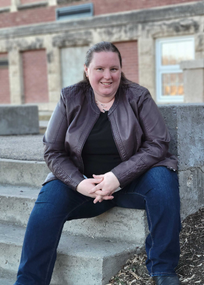 Laura Jensen wearing a brown coat and jeans sitting on a step