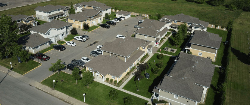 Aerial photo of the complex with 10 buildings, green space and parking lot with cars.